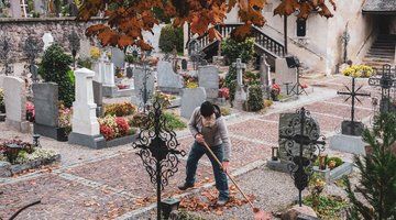 Der Friedhofswärter beim Zusammenrechen vom Laub