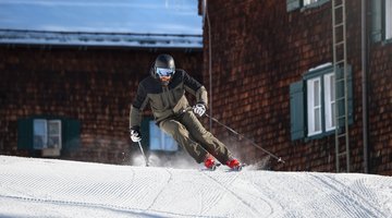 Mann beim Skifahren vor einer Skihütte