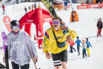 Ein Paar in bunten Outfits geht der Skipiste entlang