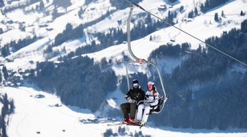 Paar fährt mit einem 2er Sessellift zum Skifahren auf die Bichlalm